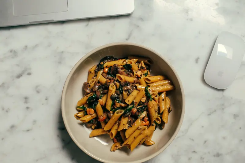 Ciotola di penne con verdure su una scrivania, accanto al mouse