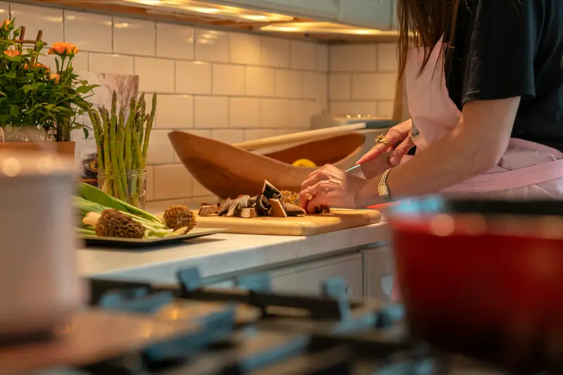 Mani che preparano asparagi e funghi su un tagliere in una cucina di casa