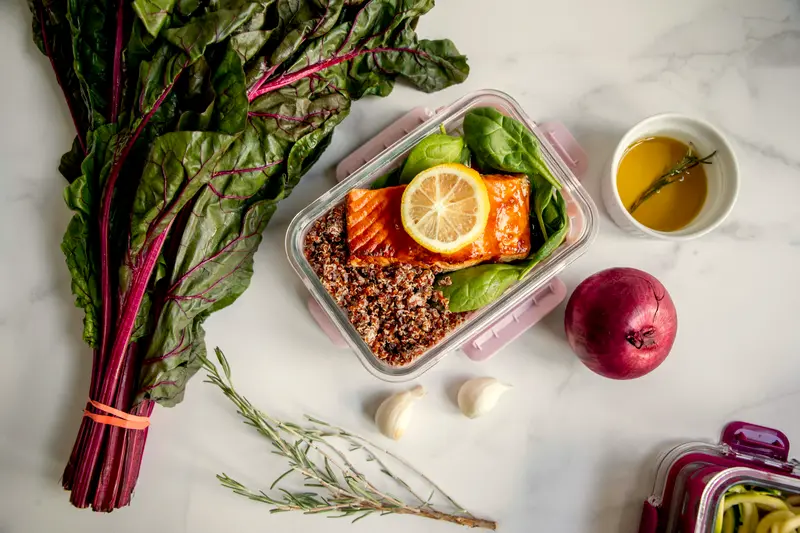 Contenitore in vetro con salmone, quinoa e limone accanto a bietole fresche