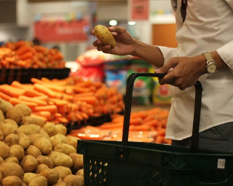 Una persona sceglie le patate al supermercato con il cestino in mano